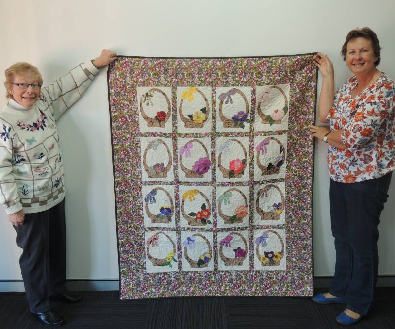 Coral Ball and Vicki Gill display a quilt  all members of the Macleay Valley Quilters contributed to with hand-stitching. The quilt be be raffled off at the Biennial Quilt Show.