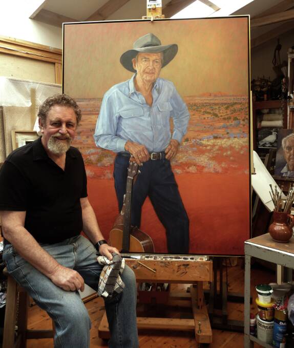 Portrait artist Bob Baird sits in front of his painting of the great country music singer Slim Dusty.